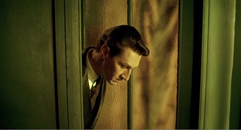 Movie still from “Delicatessen” (1991), directed by Marc Caro – A man in a suit leaning against a wall; Medium shot, Low angle