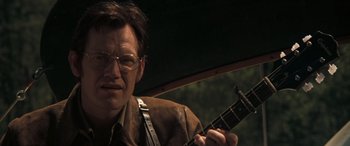 Movie still from “Deliverance” (1972), directed by John Boorman – A man holding a guitar while sitting in a car; Close Up shot, Low angle