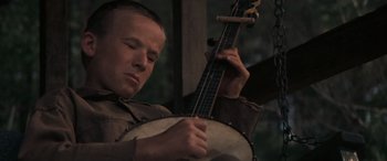 Movie still from “Deliverance” (1972), directed by John Boorman – A young man playing a banjo in front of trees; Close Up shot, Low angle
