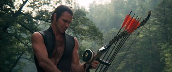 Movie still from “Deliverance” (1972), directed by John Boorman – A man holding a bow and arrow while standing in the woods; Medium shot, Low angle