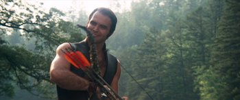 Movie still from “Deliverance” (1972), directed by John Boorman – A man holding a bow and arrow in the woods; Medium shot, Over the shoulder angle
