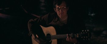 Movie still from “Deliverance” (1972), directed by John Boorman – A man playing a guitar in a dark room; Close Up shot, Over the shoulder angle