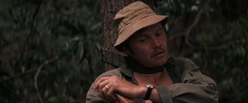 Movie still from “Deliverance” (1972), directed by John Boorman – A man in a hat is leaning against a tree; Close Up shot, High angle