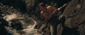 Movie still from “Deliverance” (1972), directed by John Boorman – A shirtless man climbing a rock wall near a waterfall; Medium shot, Low angle
