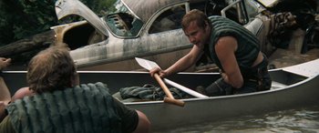 Movie still from “Deliverance” (1972), directed by John Boorman – A man in a boat holding a paddle and another man in a car; Medium shot, High angle