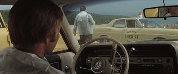 Movie still from “Deliverance” (1972), directed by John Boorman – A man standing on the side of the road next to a car; Wide shot, Over the shoulder angle