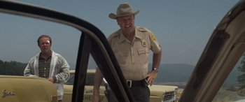 Movie still from “Deliverance” (1972), directed by John Boorman – A police officer standing next to a patrol car; Medium shot, Over the shoulder angle