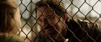 Movie still from “Den of Thieves” (2018), directed by Christian Gudegast – A man with a beard looking through a chain link fence; Close Up shot, Over the shoulder angle