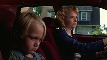 Movie still from “Dennis the Menace” (1993), directed by Nick Castle – A woman sitting in the back seat of a car with a young boy in the back seat; Close Up shot, Low angle