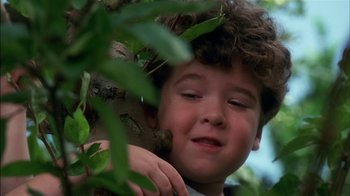 Movie still from “Dennis the Menace” (1993), directed by Nick Castle – A young boy is hiding behind a tree branch; Close Up shot, Low angle