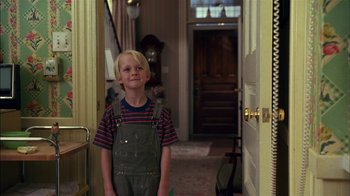 Movie still from “Dennis the Menace” (1993), directed by Nick Castle – A young boy standing in front of a doorway; Medium shot, Low angle