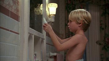 Movie still from “Dennis the Menace” (1993), directed by Nick Castle – A young boy holding a spray bottle in front of an open window; Close Up shot, Over the shoulder angle