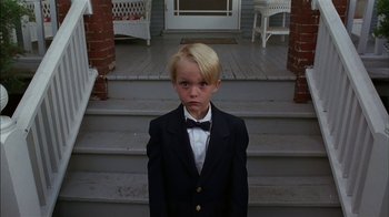 Movie still from “Dennis the Menace” (1993), directed by Nick Castle – A boy in a suit and bow tie standing in front of a porch; Medium shot, Low angle