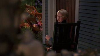 Movie still from “Dennis the Menace” (1993), directed by Nick Castle – A little girl sitting in a chair outside of a house; Medium shot, Over the shoulder angle