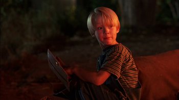 Movie still from “Dennis the Menace” (1993), directed by Nick Castle – A young boy sitting on the ground holding a book; Close Up shot, High angle