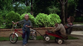 Movie still from “Dennis the Menace” (1993), directed by Nick Castle – A young boy standing next to a red wagon; Wide shot, High angle