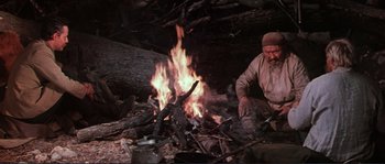 Movie still from “Dersu Uzala” (1975), directed by Akira Kurosawa – A man sitting in front of a fire in the woods; Medium shot, High angle