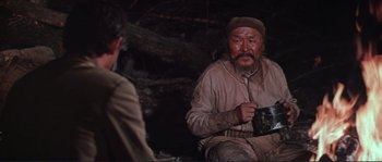 Movie still from “Dersu Uzala” (1975), directed by Akira Kurosawa – An old man sitting on the ground holding a cup; Medium shot, Over the shoulder angle