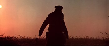 Movie still from “Dersu Uzala” (1975), directed by Akira Kurosawa – A man walking in a field at sunset with a briefcase; Close Up shot, Low angle