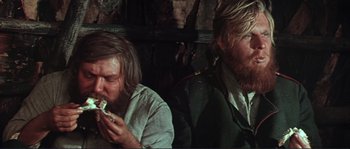 Movie still from “Dersu Uzala” (1975), directed by Akira Kurosawa – Two men sitting next to each other eating food; Close Up shot, Low angle