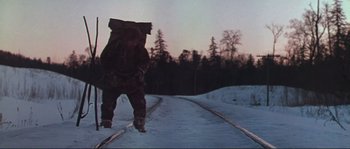 Movie still from “Dersu Uzala” (1975), directed by Akira Kurosawa – A man with a backpack walking across a snow covered road; Wide shot, Low angle