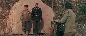 Movie still from “Dersu Uzala” (1975), directed by Akira Kurosawa – Two men dressed in military uniforms are standing in front of a camera; Wide shot, Low angle