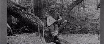 Movie still from “Dersu Uzala” (1975), directed by Akira Kurosawa – An old man sitting on a tree holding an instrument; Wide shot, Low angle