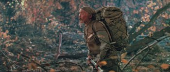 Movie still from “Dersu Uzala” (1975), directed by Akira Kurosawa – An older man with a beard and a backpack walking through the woods; Medium shot, Low angle