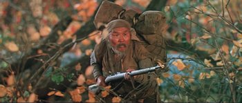 Movie still from “Dersu Uzala” (1975), directed by Akira Kurosawa – An old man with a backpack and a rifle in a tree; Medium shot, Low angle