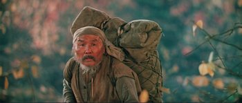 Movie still from “Dersu Uzala” (1975), directed by Akira Kurosawa – An old man with a beard and a hat is carrying a large backpack; Medium shot, Low angle