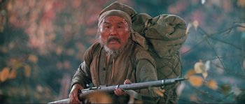 Movie still from “Dersu Uzala” (1975), directed by Akira Kurosawa – An old man with a beard and a rifle in his hand; Medium shot, Low angle