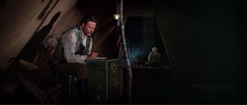 Movie still from “Dersu Uzala” (1975), directed by Akira Kurosawa – A man sitting in front of a tent writing on a piece of paper; Medium shot, Low angle