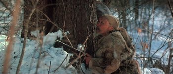 Movie still from “Dersu Uzala” (1975), directed by Akira Kurosawa – A man in a fur coat is sitting next to a tree in the snow; Medium shot, Low angle