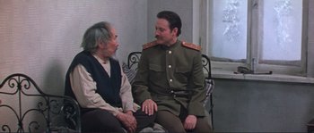 Movie still from “Dersu Uzala” (1975), directed by Akira Kurosawa – Two men sitting on a bench talking to each other; Medium shot, High angle