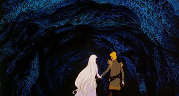 Movie still from “The Last Unicorn” (1982), directed by Jules Bass – A couple of people standing next to each other in front of a cave; Wide shot, Low angle