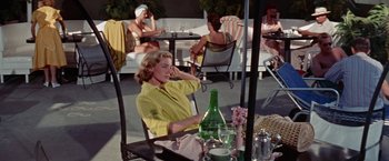 Movie still from “Designing Woman” (1957), directed by Vincente Minnelli – A woman sitting at an outdoor table talking on the phone; Medium shot, High angle