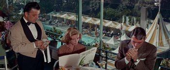 Movie still from “Designing Woman” (1957), directed by Vincente Minnelli – A woman sitting at an outdoor table reading a menu; Medium shot, High angle