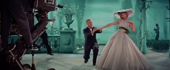 Movie still from “Designing Woman” (1957), directed by Vincente Minnelli – A man kneeling down next to a woman in a white dress; Wide shot, Low angle