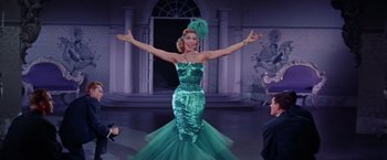 Movie still from “Designing Woman” (1957), directed by Vincente Minnelli – A woman in a green dress is standing in front of a crowd; Medium shot, Low angle