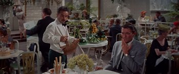 Movie still from “Designing Woman” (1957), directed by Vincente Minnelli – A man standing in front of a bunch of fruit; Medium shot, Over the shoulder angle