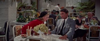 Movie still from “Designing Woman” (1957), directed by Vincente Minnelli – A man and a woman sitting at a table with grapes; Medium shot, Over the shoulder angle