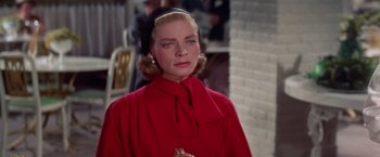 Movie still from “Designing Woman” (1957), directed by Vincente Minnelli – A woman in a red coat is standing in front of a brick wall; Close Up shot, Over the shoulder angle