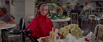 Movie still from “Designing Woman” (1957), directed by Vincente Minnelli – A woman sitting at a table with a plate of food on top of it; Medium shot, Over the shoulder angle
