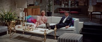 Movie still from “Designing Woman” (1957), directed by Vincente Minnelli – A man and a woman sitting on a white couch; Wide shot, High angle