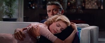 Movie still from “Designing Woman” (1957), directed by Vincente Minnelli – A man and a woman hugging each other in front of a window; Medium shot, Low angle
