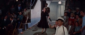 Movie still from “Designing Woman” (1957), directed by Vincente Minnelli – A woman in a black dress and a man in a brown suit; Wide shot, High angle