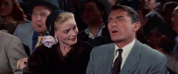 Movie still from “Designing Woman” (1957), directed by Vincente Minnelli – A man and a woman are standing together in front of a group of people; Close Up shot, Low angle