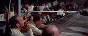 Movie still from “Designing Woman” (1957), directed by Vincente Minnelli – A group of people sitting in a room with papers in front of them; Medium shot, High angle