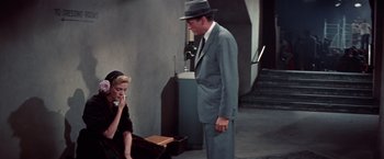 Movie still from “Designing Woman” (1957), directed by Vincente Minnelli – A man in a suit and a hat standing next to a woman in a black dress; Medium shot, High angle