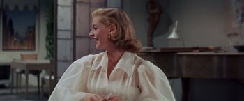 Movie still from “Designing Woman” (1957), directed by Vincente Minnelli – A woman in a white dress smiling at the camera; Medium shot, Over the shoulder angle
